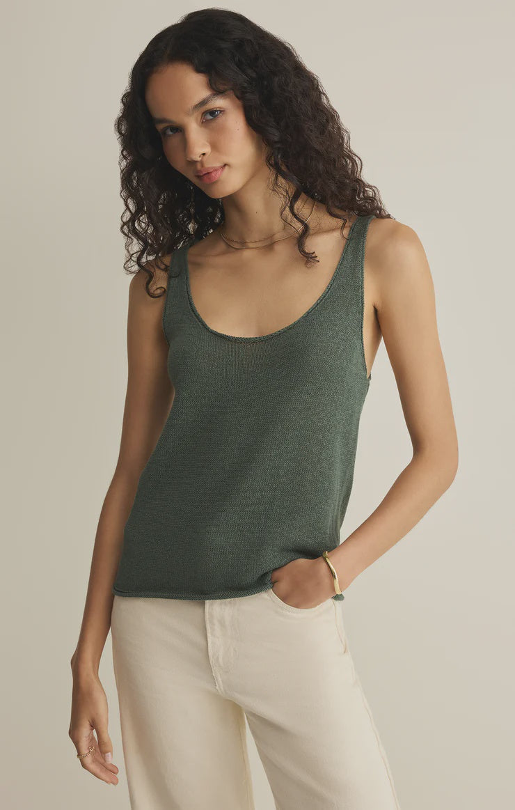 A person with long curly hair wears the Zertz PERCH SWEATER TANK in forest green and cream-colored pants, standing against a plain light background with one hand in their pocket.