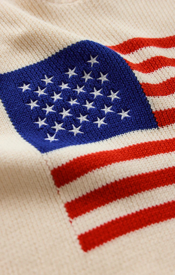 Close-up of the Zertz SLEEVLESS PATRIOT SWEATER, a cream cotton knit with an American flag design in blue, white stars, and red stripes—ideal as a patriotic summer sweater.