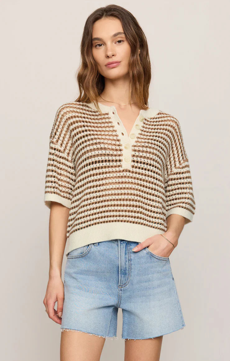 A woman wears the Zertz KYLO STRIPED SWEATER—a lightweight, short-sleeve crochet-knit with stripes—paired with high-waisted light blue denim shorts, standing against a plain light background.