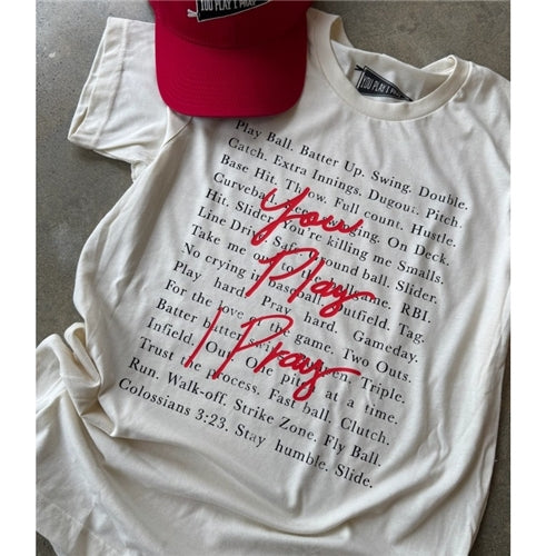 The "You Play, I Pray Tee" by Loca on Main features a cream base with popular baseball sayings in black and "You Play I Pray" in bold red script on the front—perfect to pair with a red cap.