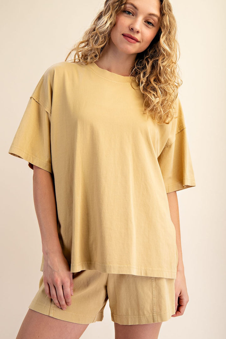 A woman with curly blonde hair is wearing The Mellow Yellow Set by Loca on Main—an everyday lounge set featuring a loose-fitting, mineral-washed tee and relaxed fit shorts. She stands smiling softly against a neutral background.