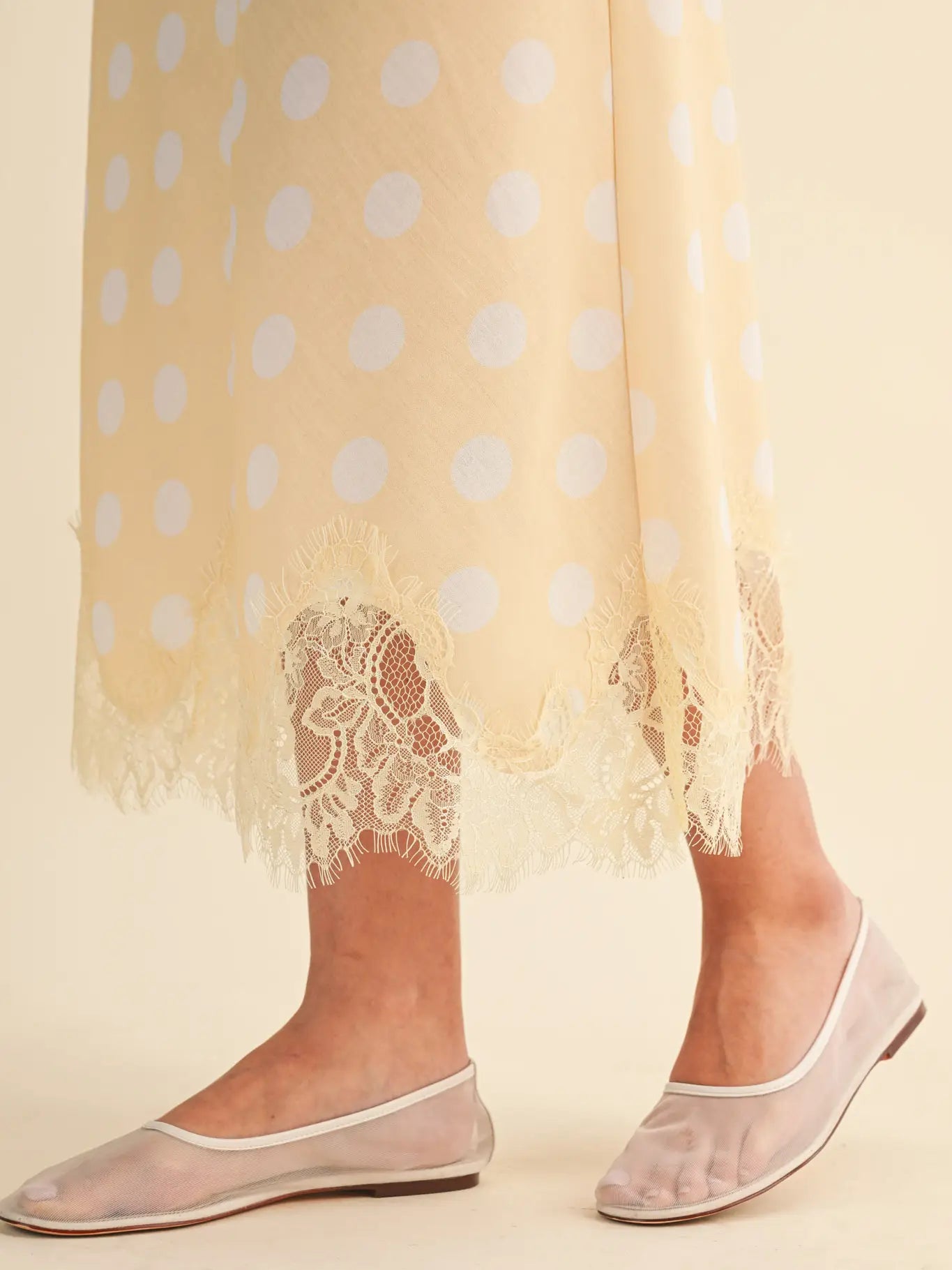 A person wearing the Zertz POLKA DOT LACE TRIM SKIRT stands on a beige surface, shown from mid-calf down, paired with sheer light pink ballet flats featuring delicate white trim.