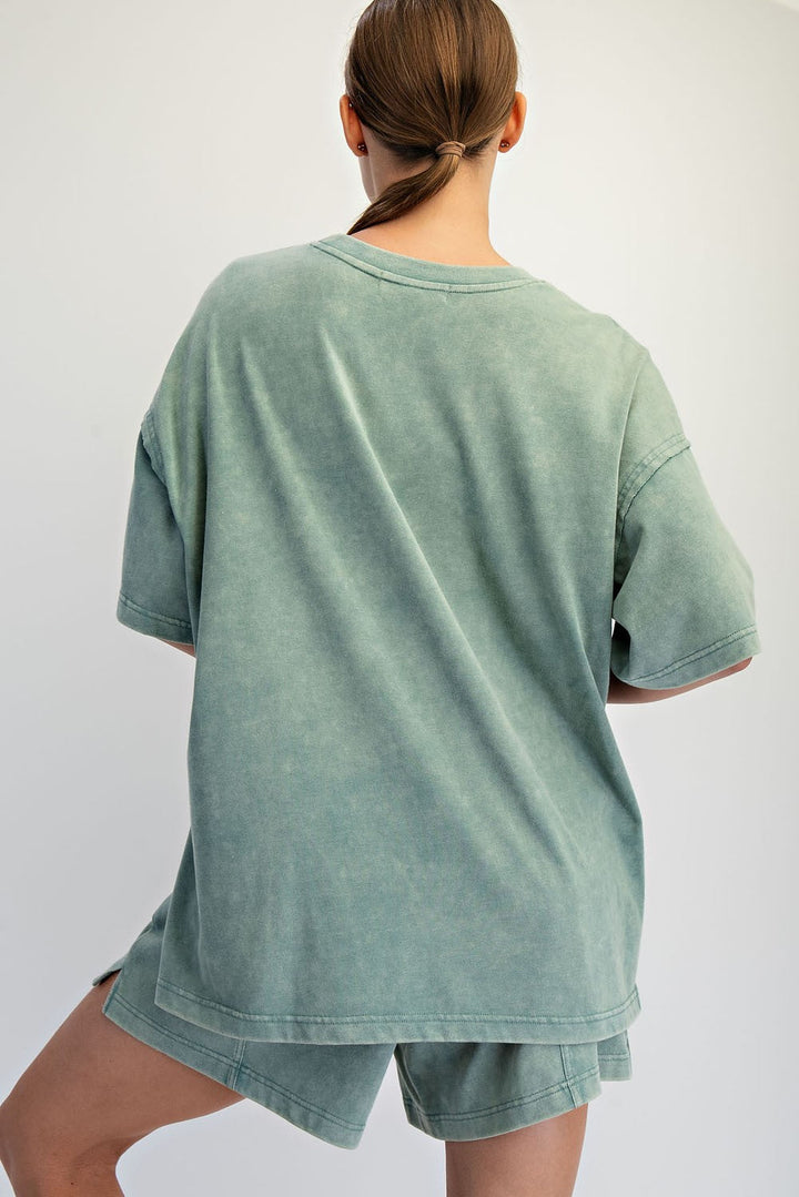 A person with brown hair in a low ponytail models The Mellow Yellow Set by Loca on Main—mineral washed tee and relaxed fit shorts—standing with their back to the camera against a plain light background: perfect everyday loungewear.