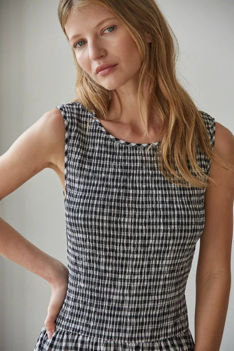 A woman with long blonde hair wears the Zertz SAYLER GINGHAM SMOCKED DRESS in black and white. She stands indoors, looking at the camera with a relaxed expression, her left hand resting on her hip.