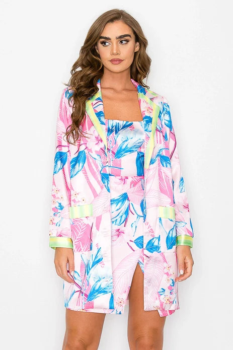 A woman with long brown hair wears the Zertz FLORAL PRINTED SHIRT DRESS featuring blue and green tropical leaf and flower prints, standing against a white background.