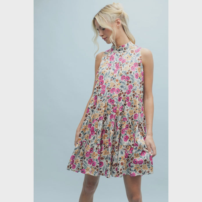 A woman models the Zertz SLVLESS PATTERN DRESS, a sleeveless, high-neck mini dress with an A-line silhouette and tiered skirt, standing against a light blue background and smiling gently.