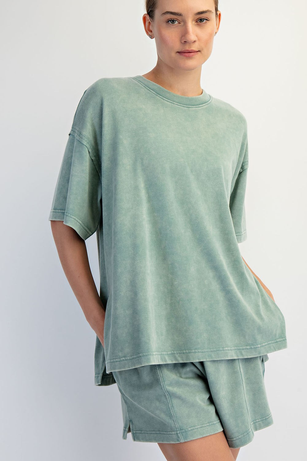 A woman models The Mellow Yellow Set by Loca on Main—an everyday loungewear look featuring a loose-fitting, mineral washed tee in light green with matching relaxed fit shorts, hands in pockets and a neutral expression against a plain background.