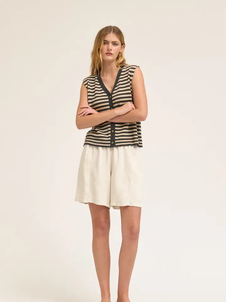 A woman stands with arms crossed, wearing Zertz TENCEL SHORTS made from sustainable fabric and a black and beige striped sleeveless button-up top, set against a plain light background.