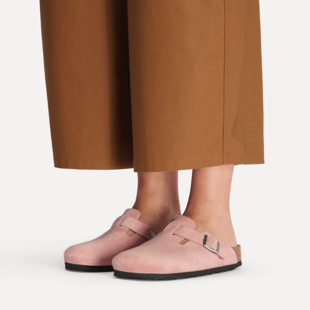 A person in wide-legged brown pants wears Zertz BOSTON LEVE PINK CLAY N clogs with buckles. The light pink shoes have a contoured footbed, soft suede-like texture, and black soles, standing on a white background.