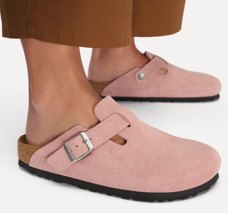 A person in light brown pants wears Zertz BOSTON LEVE PINK CLAY N clogs, crafted from soft suede with a silver buckle, black soles, and a contoured footbed, standing against a white background.
