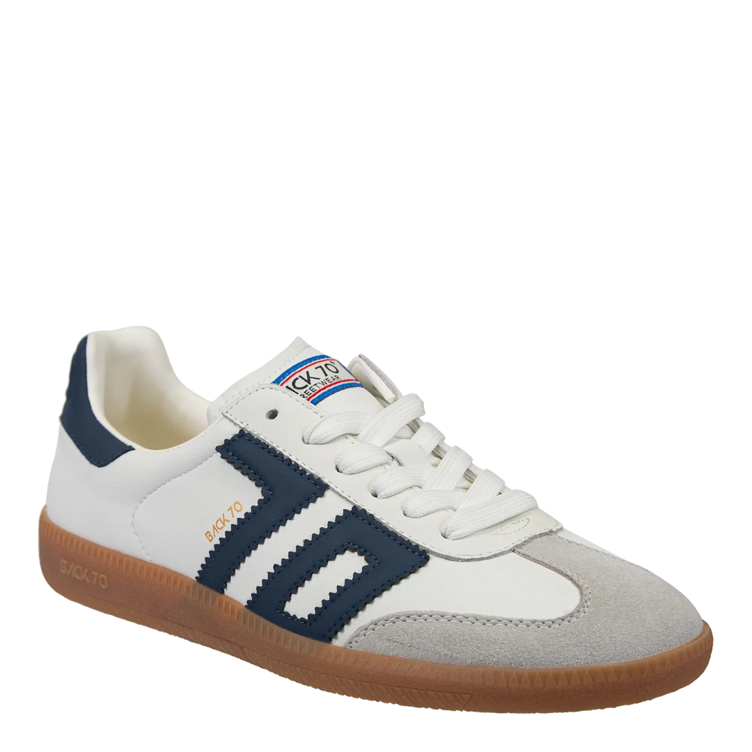 The Zertz CLOUD IN NAVY SNEAKER features a white upper with navy stripes, gray suede toe, gum sole, and white laces. The tongue sports a blue/red/white logo label, and DK-770 in gold decorates the color block side. Soccer street style inspired.