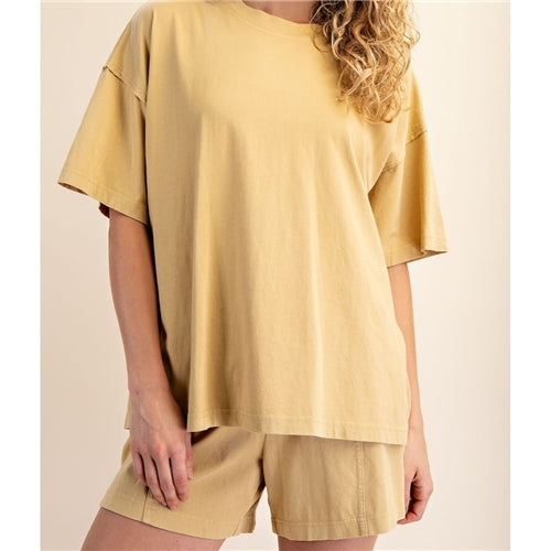 A person with wavy blonde hair models The Mellow Yellow Set by Loca on Main, featuring a mineral washed tee and relaxed beige shorts, against a neutral background. Their face is partially out of frame, highlighting this everyday lounge set.