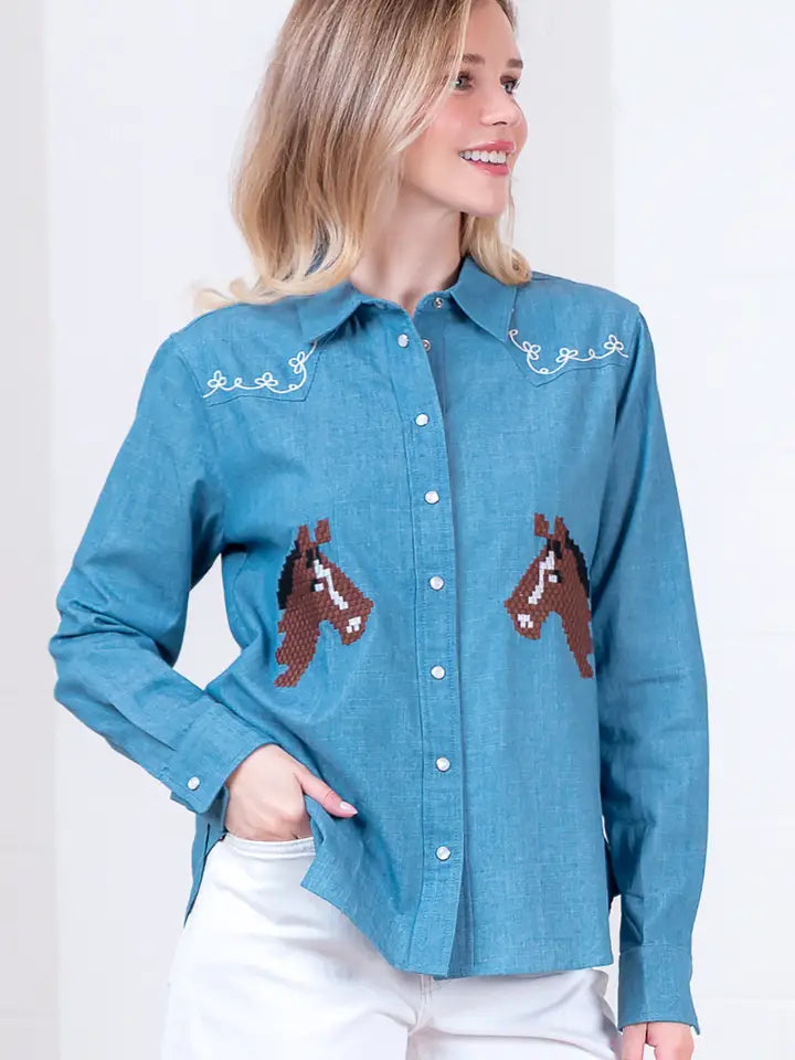 A woman models the Zertz DENIM EMBROIDERY TOP, featuring horse embroidery and white stitching near the shoulders, smiling with one hand in her pocket.