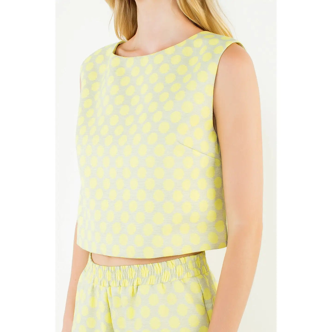 A woman wears the Zertz POLKA DOT TOP, a sleeveless, light yellow crop top with a dot pattern, paired with matching high-waisted shorts for a comfortable and casual summer look.