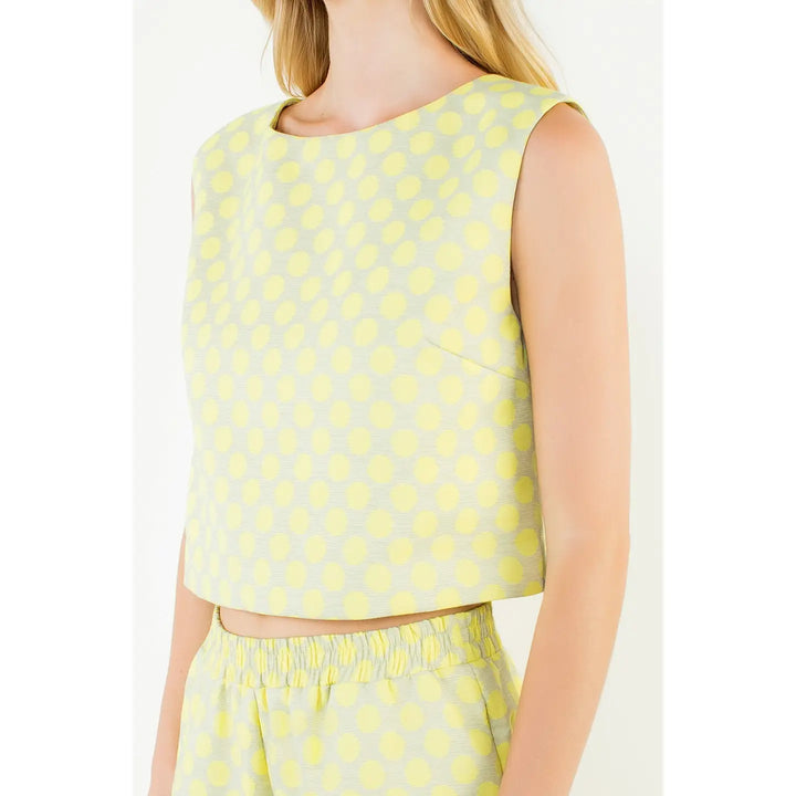 A woman wears the Zertz POLKA DOT TOP, a sleeveless, light yellow crop top with a dot pattern, paired with matching high-waisted shorts for a comfortable and casual summer look.