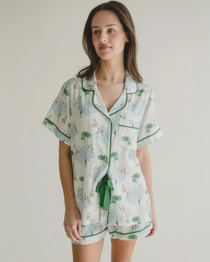 A woman with long brown hair models the Zertz PALM COURTS PAJAMA SHORT SET, featuring a green and blue print, green piping, elastic waist, and green drawstring, set against a plain light background.