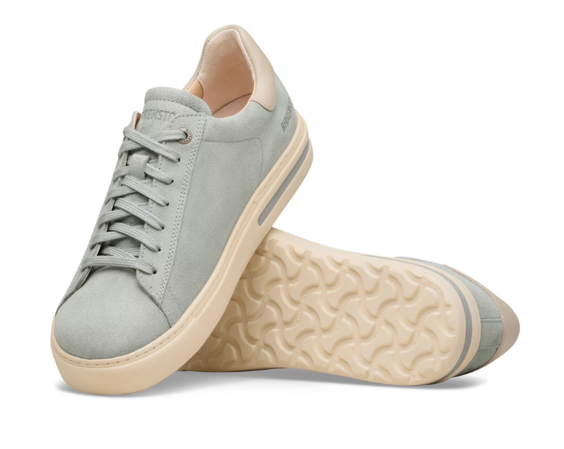 A pair of Zertz BEND LOW MIX LEVE LENA PURE SAGE NARROW FIT sneakers in light gray with beige soles—one upright and one on its side, showing the textured sole and shock-absorbing comfort for all-day wear.