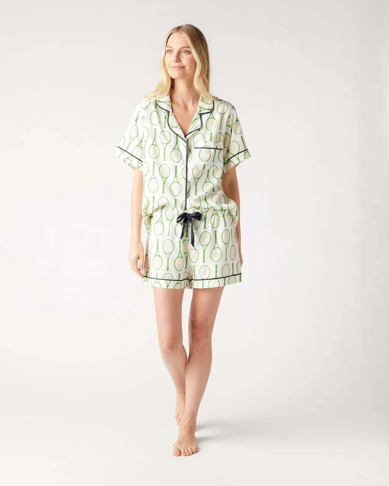 A woman stands barefoot in the Zertz TENNIS TIME PAJAMA SHORTS SET, featuring short sleeves, black piping, and a green tennis racket print, against a plain light background.