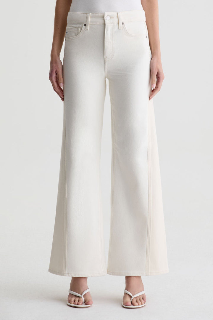 A person stands against a light background, cropped at the chest to show only the lower torso and legs, wearing Zertz SAIGE WIDE LEG MID RISE jeans in off-white paired with white heeled sandals.