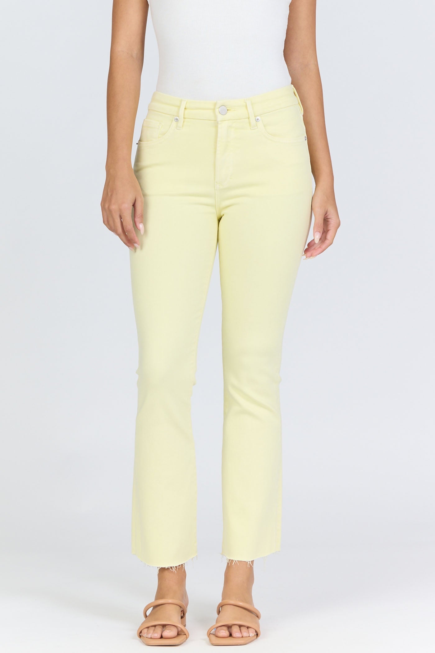 A person stands against a plain light background wearing Zertz's JEANNE JEAN yellow denim jeans with a raw hem and slim, comfortable fit, paired with a white sleeveless top and beige sandals.