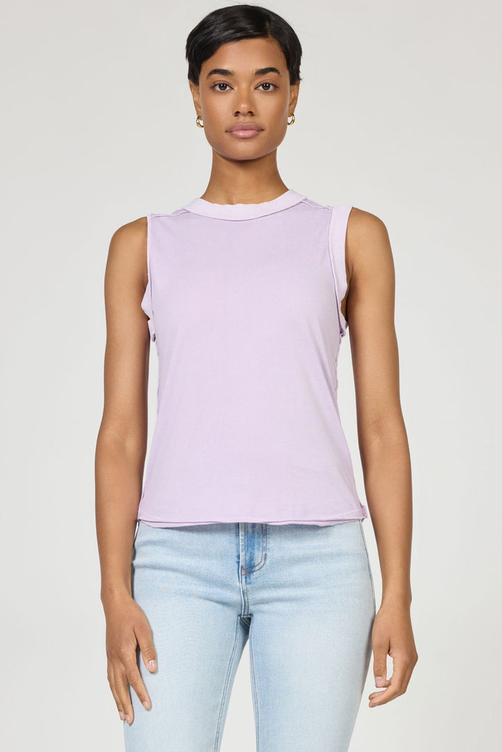 A woman with short dark hair wears the sleeveless light purple ZO TANK by Zertz and light blue jeans, standing against a plain background and looking at the camera—an essential wardrobe staple.