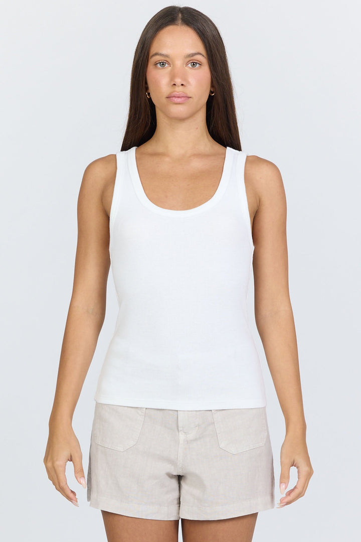 A woman with long brown hair stands facing forward, wearing the LOUISE TANK by Zertz in white and light beige shorts. Her expression is neutral, set against a plain light background.