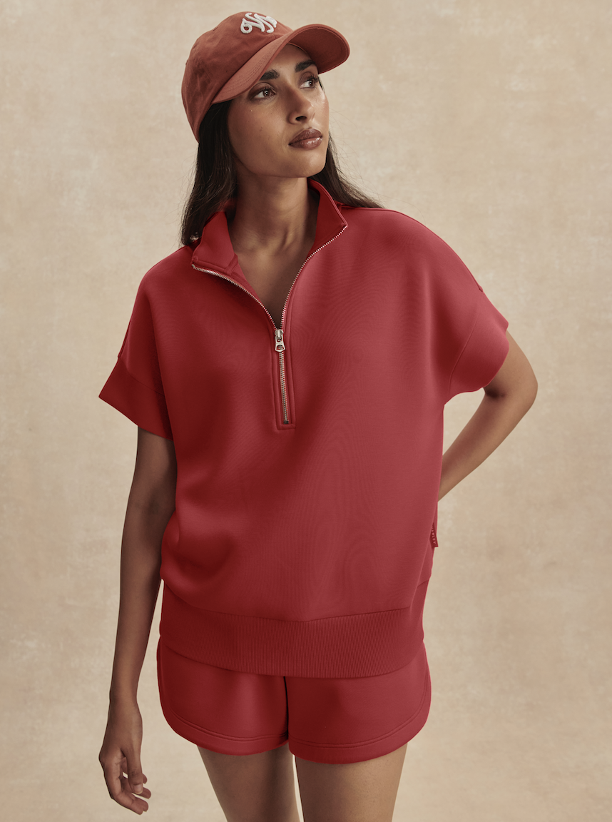 A woman in the Zertz RITCHIE SHORT SLEEVE SWEAT - RICH RASPBERRY stands against a neutral background, looking to the side with one hand behind her back—an ideal addition to any casual wardrobe.