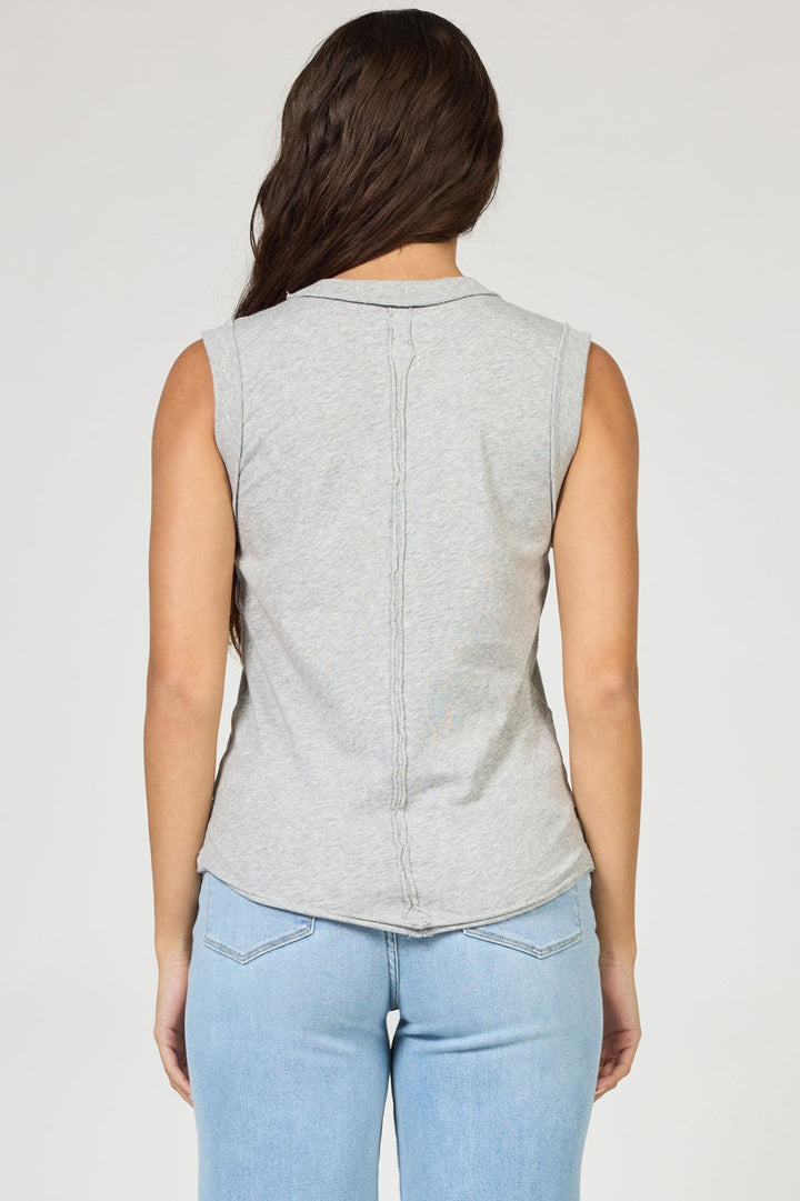 A woman with long brown hair, shown from the back against a plain light background, wears the Zertz ZO TANK—a sleeveless, light gray minimalist top—paired with light blue jeans.