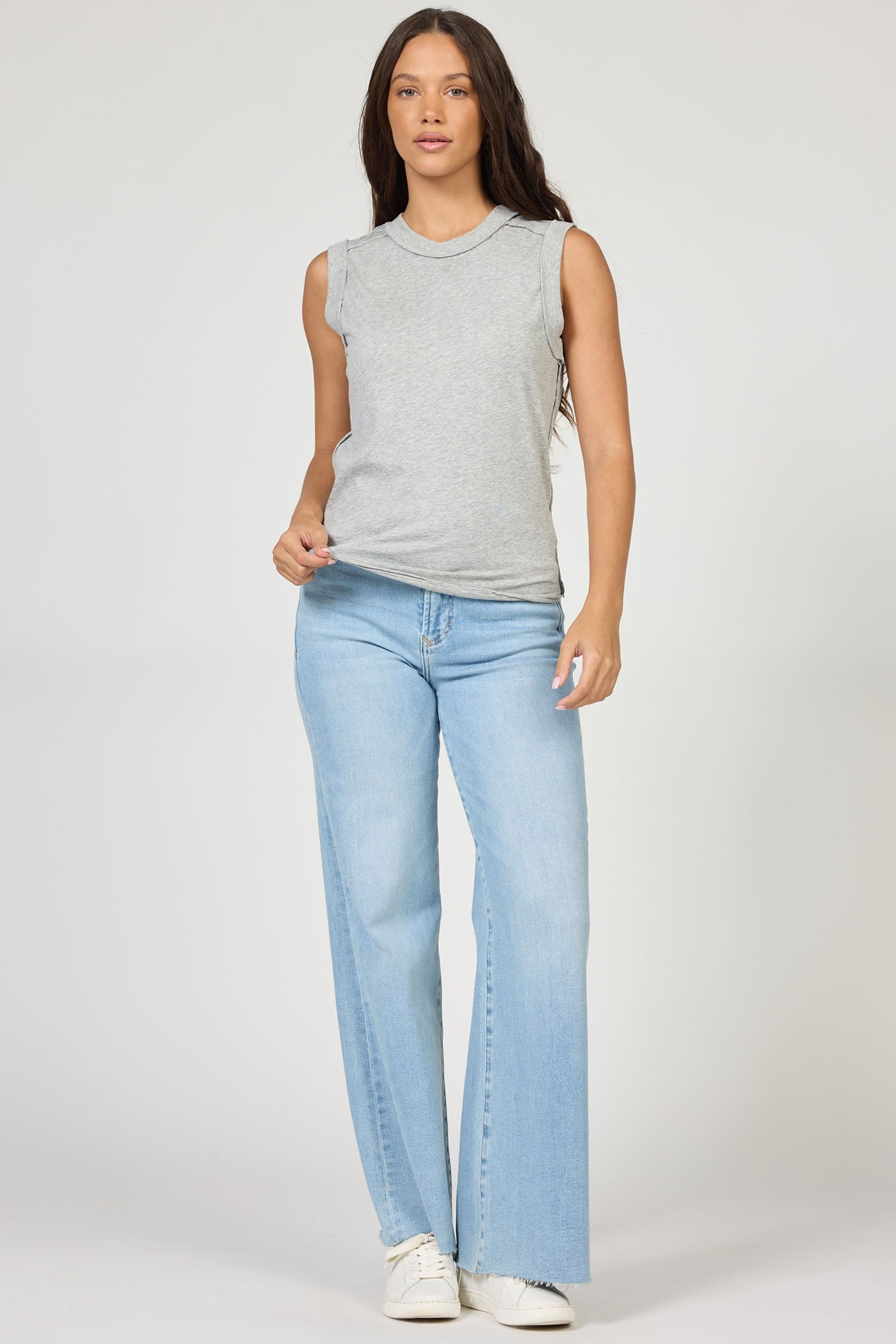 A woman with long brown hair wears the Zertz ZO TANK, paired with light blue wide-leg jeans and white sneakers. She stands facing forward against a plain light background.