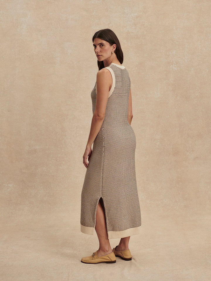 A woman with long brown hair wears the Zertz SADIA STITCH KNIT DRESS, a sleeveless, ankle-length design with beige and brown patterns and textured stitching. She stands sideways against a neutral background, tan shoes completing her look.