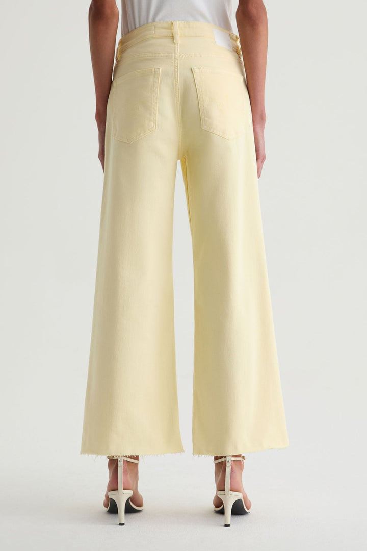 Back view of a person wearing Zertz SAIGE WIDE LEG CROP jeans in light yellow, showcasing a wide-leg silhouette, cropped raw hems, styled with white heels and a white top against a plain light background.