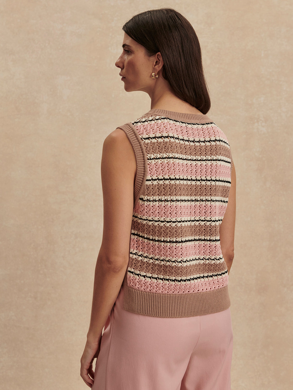 A woman with straight brown hair wears the Zertz DEELEY STRIPE TANK in Warm Taupe/Mellow Rose, paired with light pink pants, against a neutral textured background.