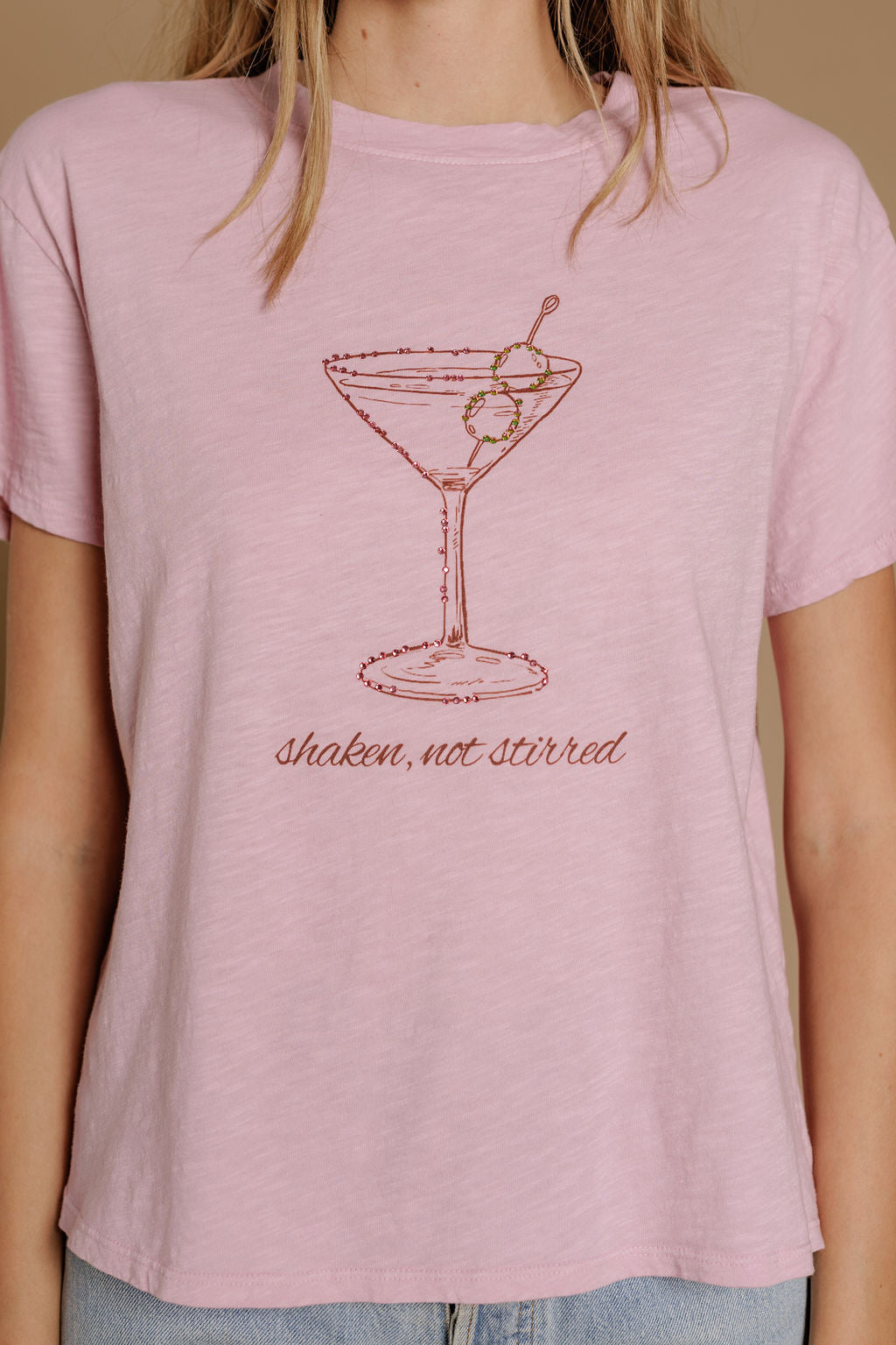 A woman wears the Zertz SHAKEN NOT STIRRED SLUB CAP TEE, a light pink top with a martini glass line drawing and “shaken, not stirred” printed beneath.