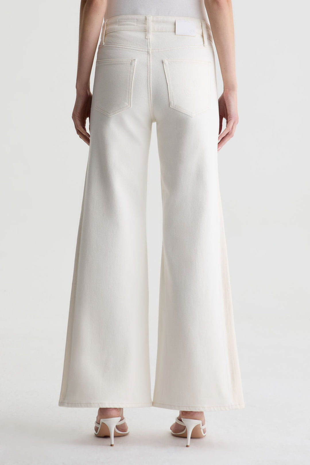 A person wearing Zertz’s SAIGE WIDE LEG MID RISE white jeans and white heeled sandals, shown from the back against a plain white background.