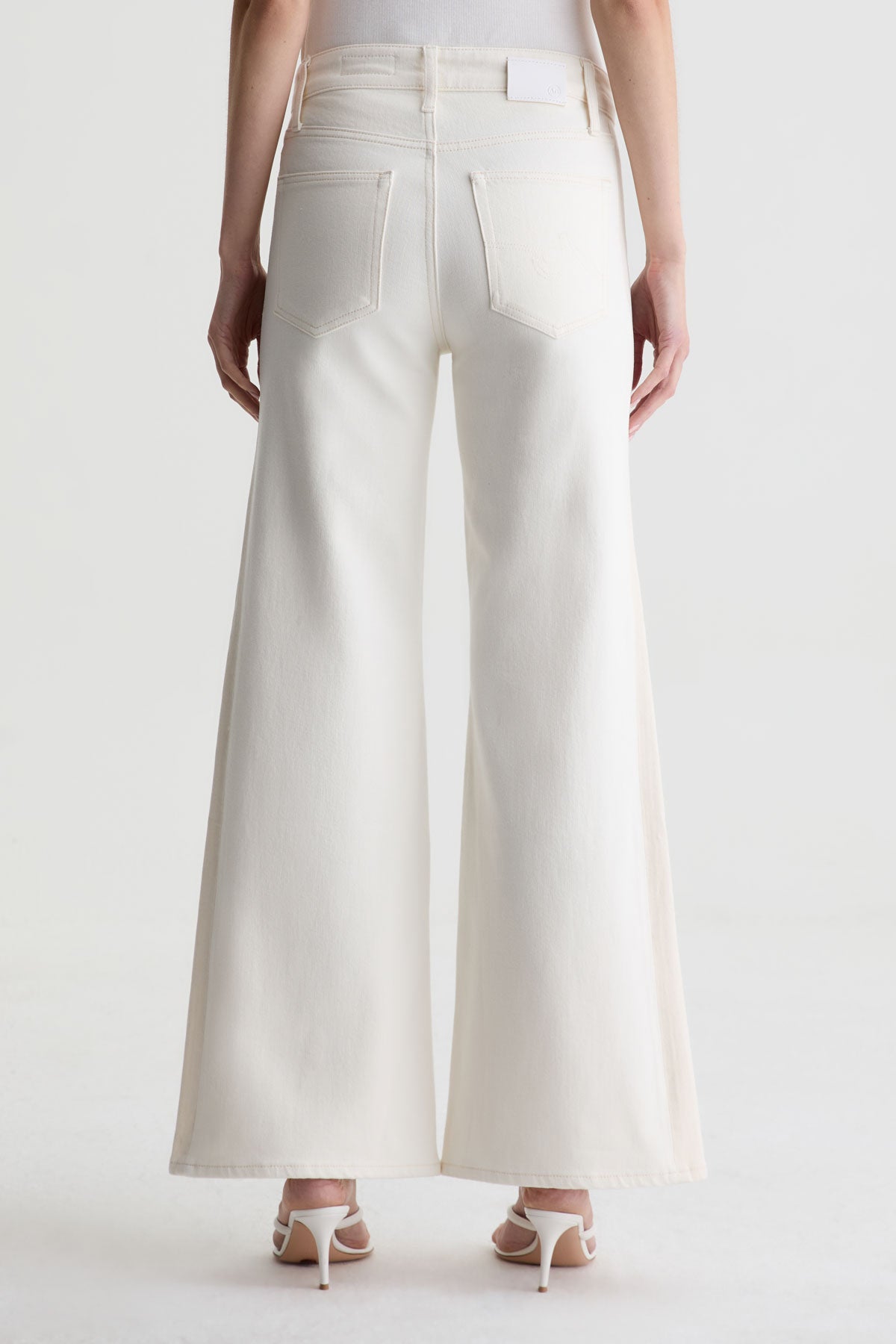 A person wearing Zertz’s SAIGE WIDE LEG MID RISE white jeans and white heeled sandals, shown from the back against a plain white background.
