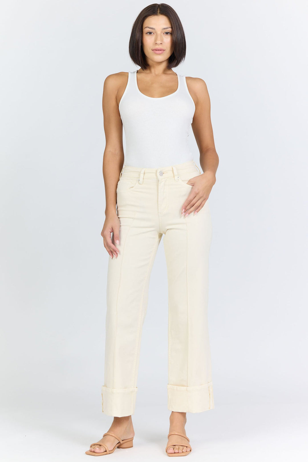 A woman with a bob haircut exudes timeless style wearing the Zertz HOLLY JEAN white tank top and cream wheat wide-leg pants, paired with beige sandals, against a plain white background.
