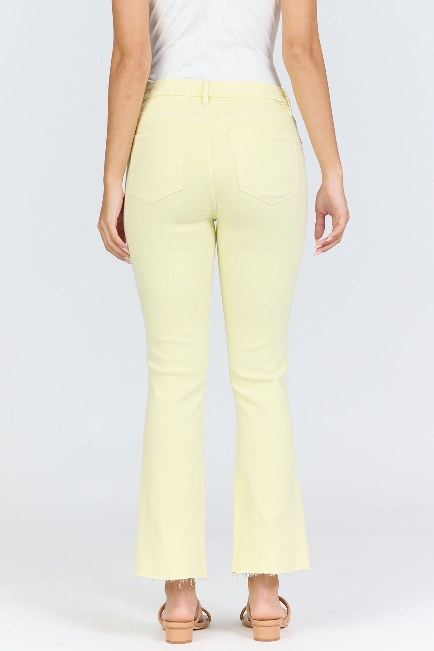 A person wearing Zertz JEANNE JEAN in pale yellow—slightly flared with raw hems, classic back pockets, and a timeless silhouette—paired with a white sleeveless top and open-toe sandals, seen from the back to show the comfy fit.