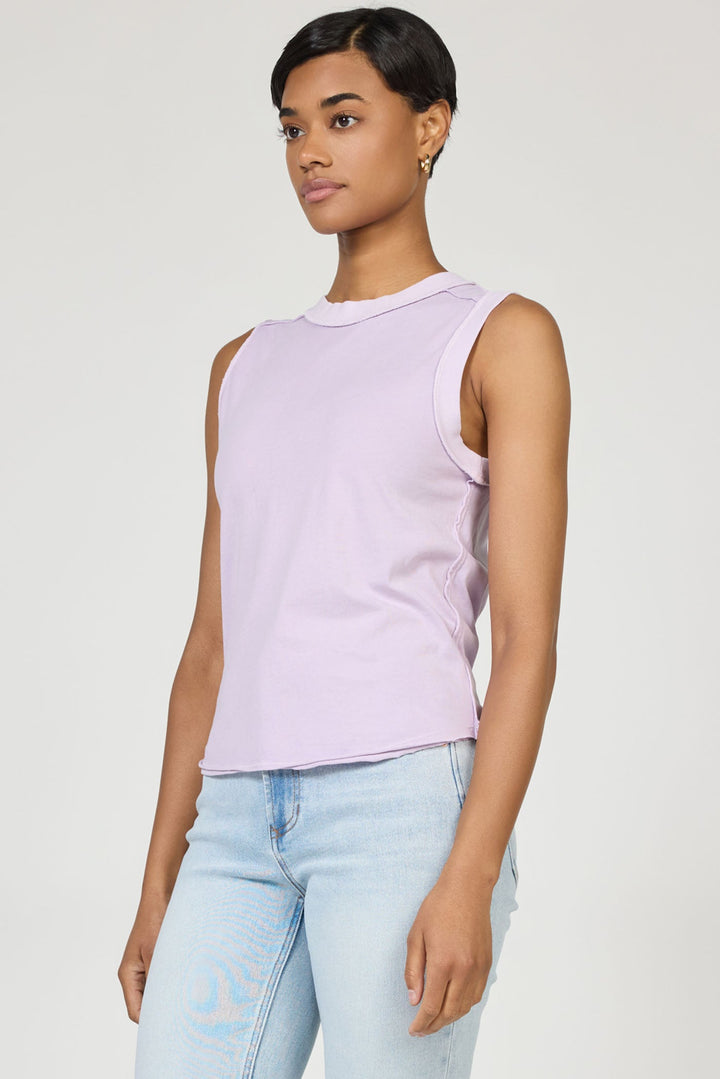 A woman with short dark hair wears a sleeveless light purple Zertz ZO TANK made of breathable fabric and light blue jeans, standing against a plain light background and looking slightly to the side with a neutral expression.