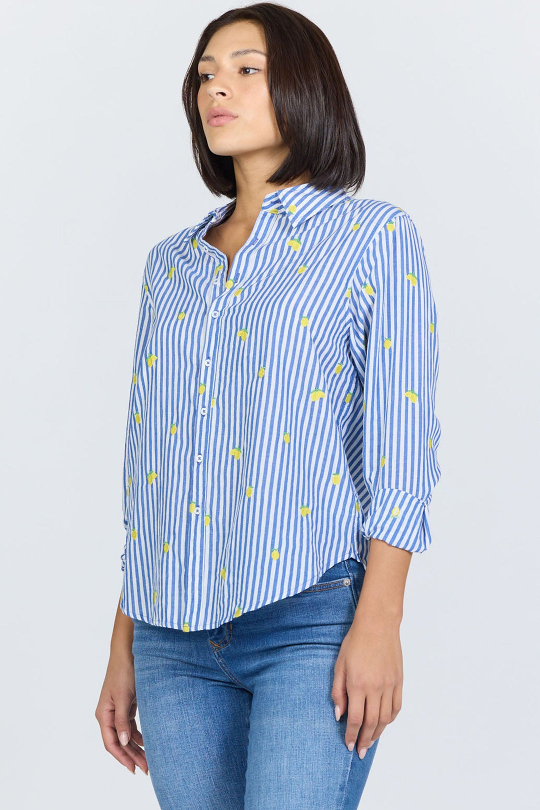 A person wears the Zertz LOLITA TOP, a blue and white vertically striped feminine blouse with yellow embroidery, paired with blue jeans, standing against a plain light background.