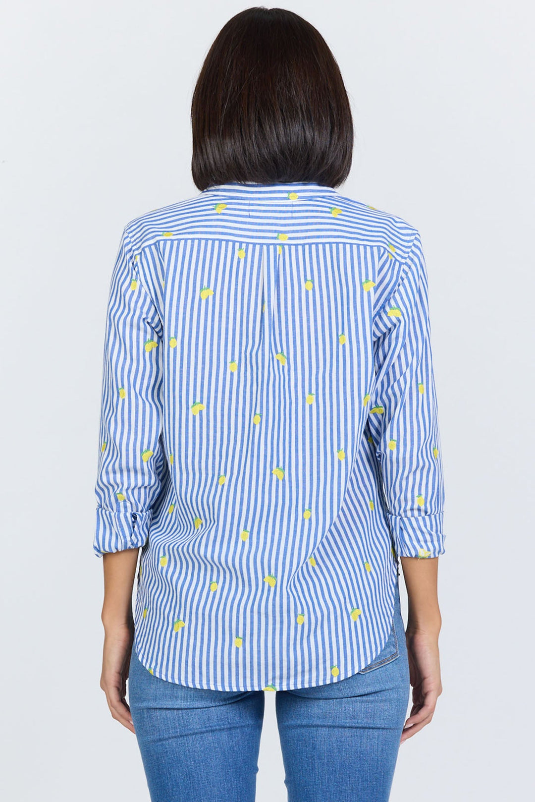 A person with shoulder-length dark hair is seen from the back wearing the Zertz LOLITA TOP—a feminine blouse with blue and white vertical stripes, small yellow dots, three-quarter sleeves—paired with blue jeans.