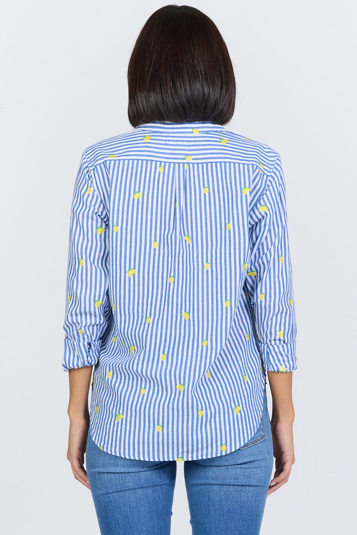 A person with shoulder-length dark hair is seen from the back wearing the Zertz LOLITA TOP—a feminine blouse with blue and white vertical stripes, small yellow dots, three-quarter sleeves—paired with blue jeans.