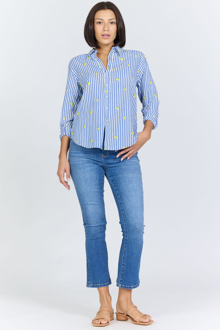 A woman faces forward wearing the Zertz LOLITA TOP—a blue and white striped feminine blouse with yellow accents—paired with blue skinny jeans and tan sandals, set against a plain light background.