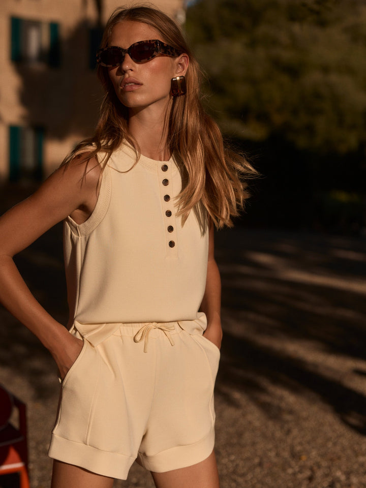 A woman stands outdoors in sunlight, hands in pockets, wearing Zertz&